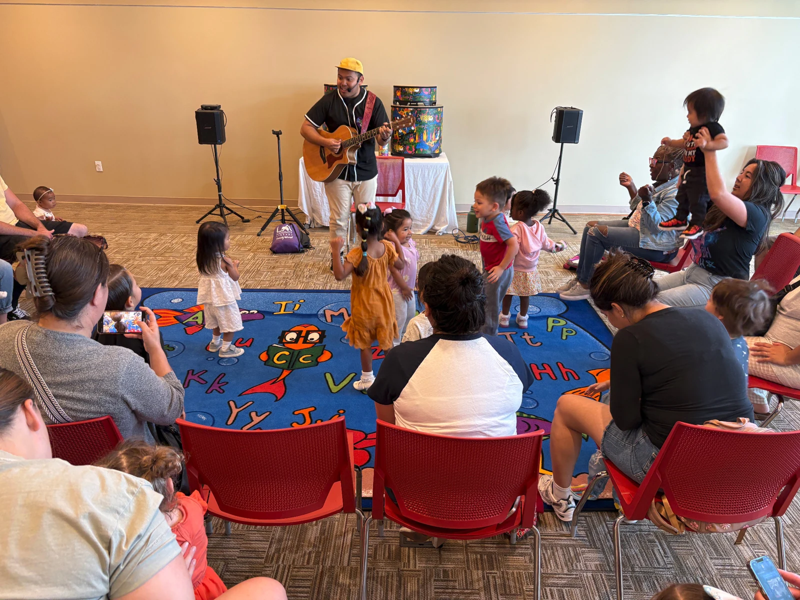 A musician playing guitar while children and families enjoy Key n Harmony